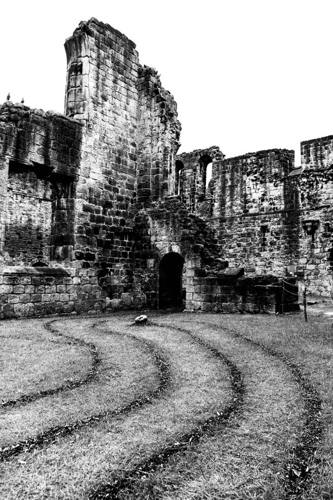 A black and white image of a ruined abbey [Kirkstall Abbey]. There is a labyrinth marked out on the grass in front of the building.