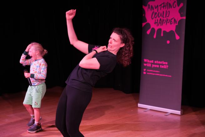 A woman strikes a crazy position while a little boy with a microphone laughs hysterically 