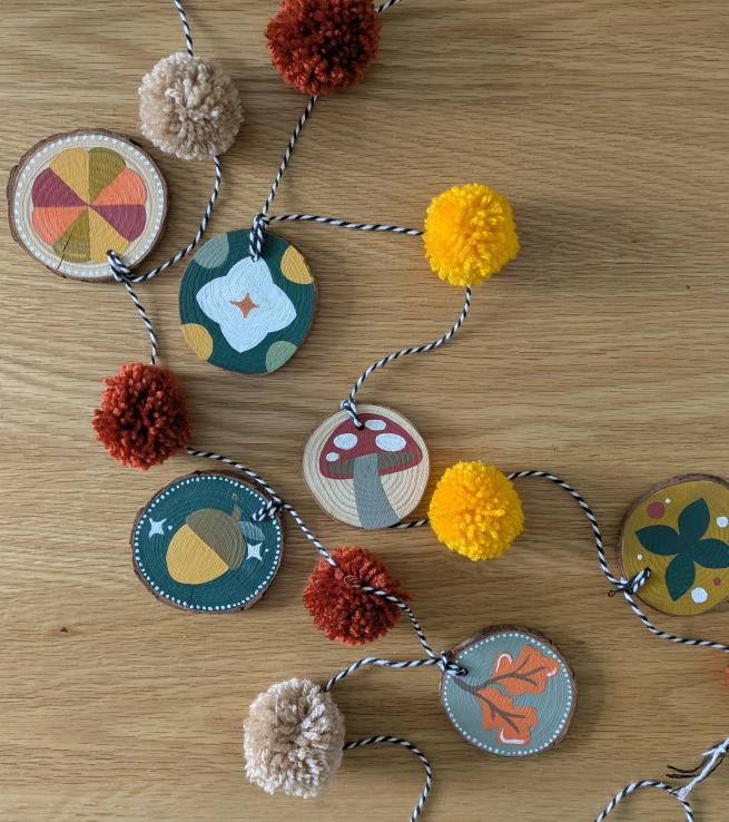 A string of pompoms and handpainted wooden pendants with Autumnal designs