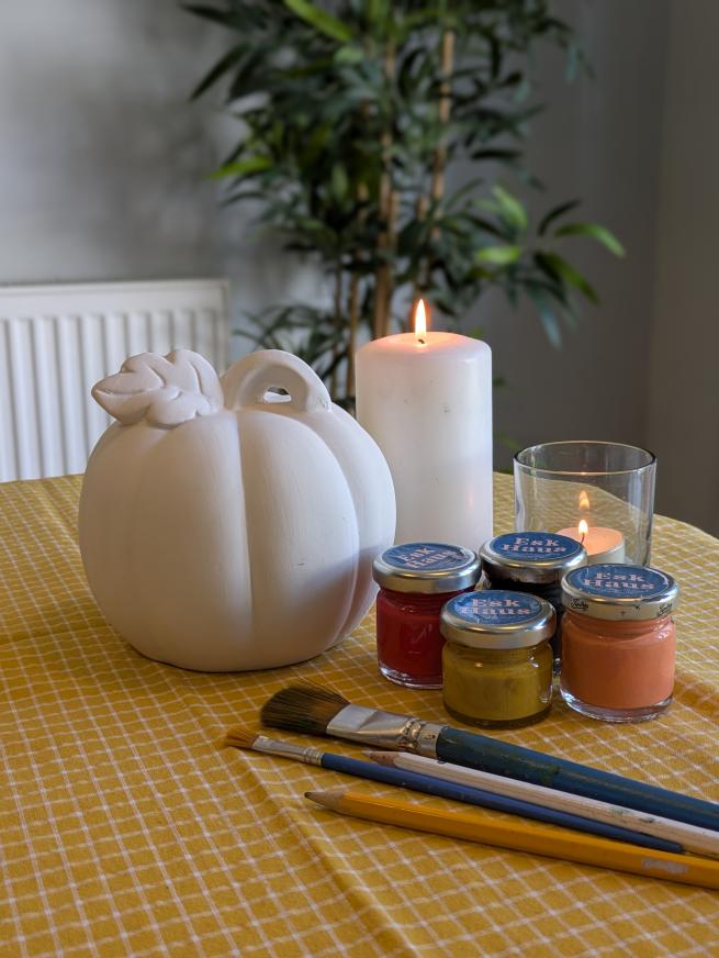 A medium ceramic pumpkin with paint pots and brushes next to it