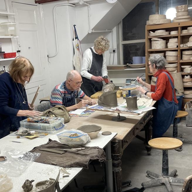 4 people around a wooden workbench, working on their clay projects