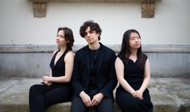 Three musicians dressed all in black sat back to back. 