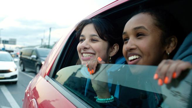Two young women peer joyfully out of the window of a car.