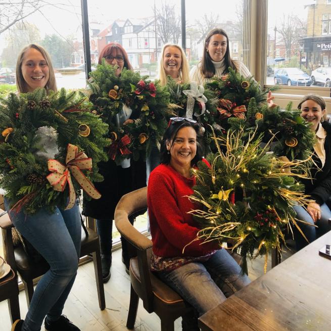 4 people stand holding their handmade wreaths and one person is sat down in front with hers.