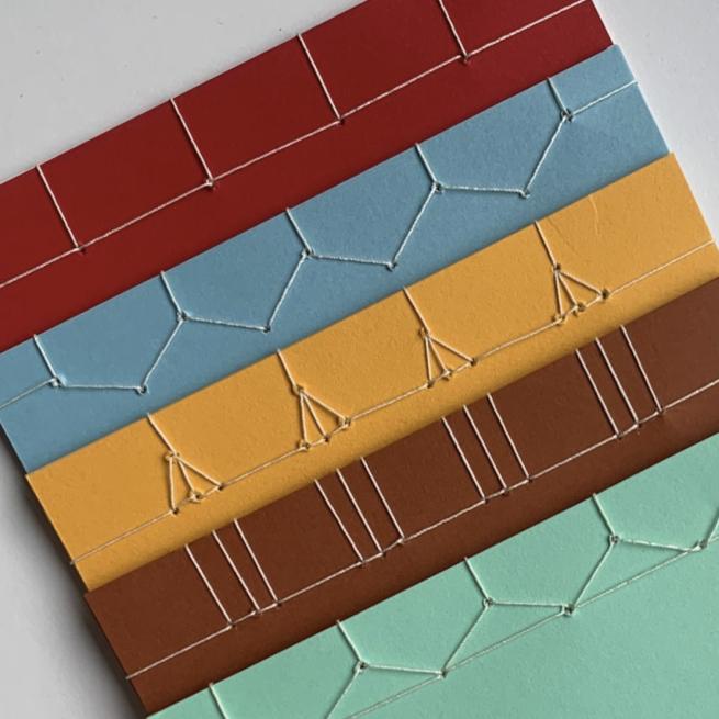 5 different colour books lay on top of each other, each with a different style binding on the edge.