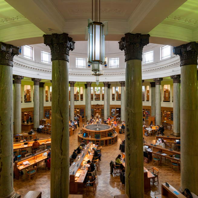 A view looking over a round library reading room with green stone columns and a hanging chandelier.