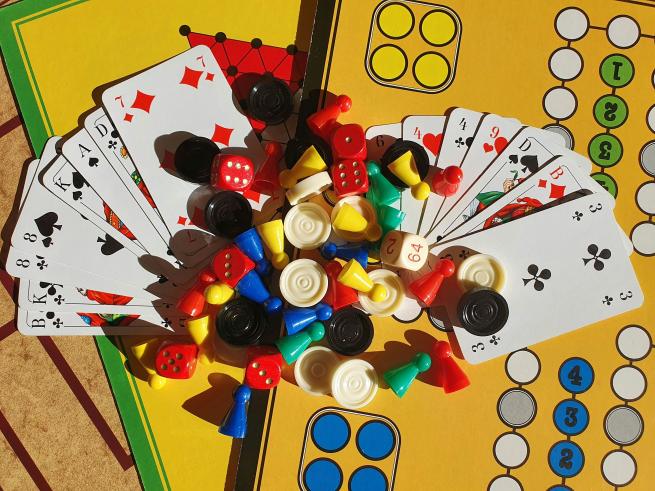 A variety of playing cards is splayed across two game boards, with a collection of dice and counters.