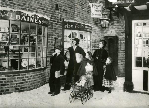 A black and white photograph of a family browsing a recreated Victorian street scene covered in snow (Abbey House Museum).