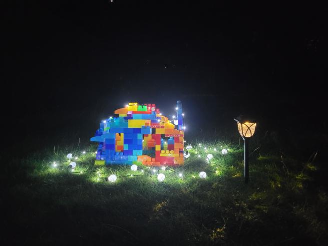Colorful toy block house illuminated by garden lights on grass at night with starry sky above