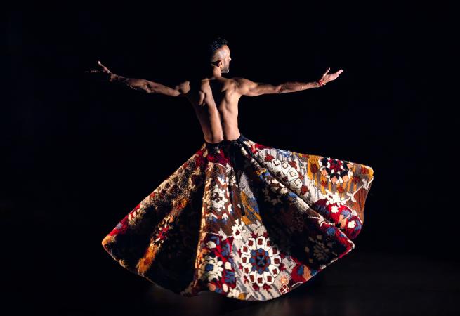 A man stands with his back to the camera wearing traditional dress while dancing