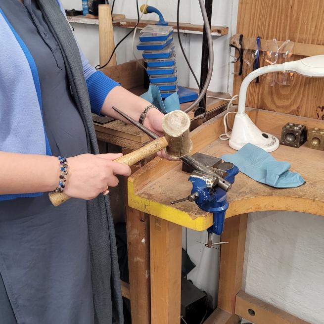 Someone using a hammer to shape a silver ring on a mandril