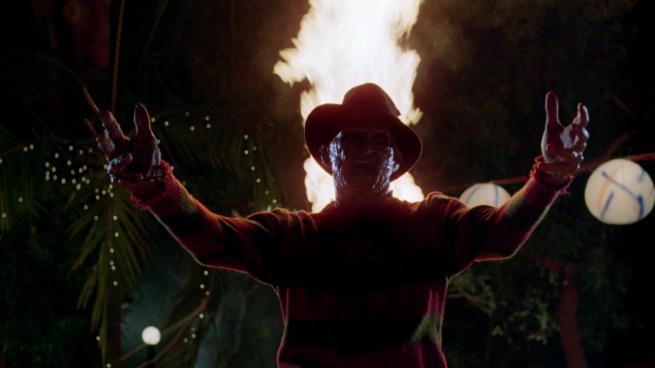 Freddy Krueger stands with his arms outstretched in front of a fire