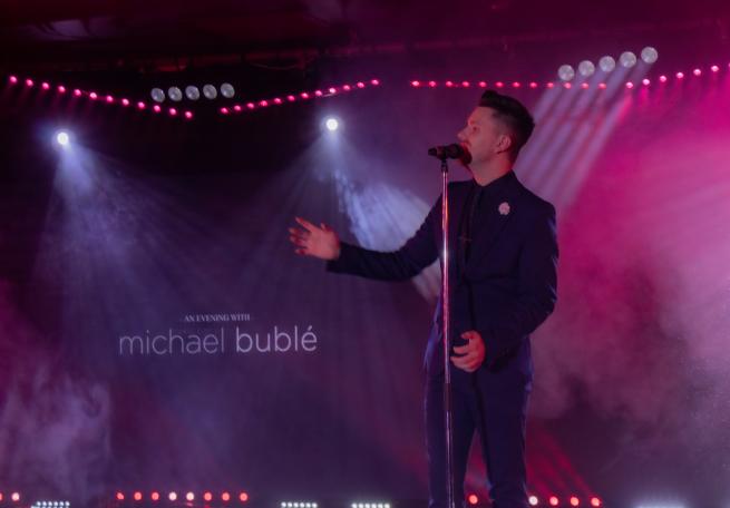 A singer performs in a dark room, smoke and purple lighting create a festive atmosphere