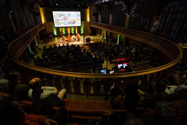 A large audience watches a panel discussion in the Howard Assembly Room.