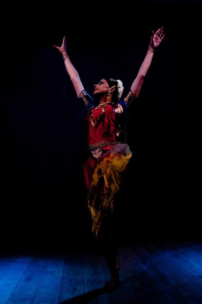 Picture showing an Indian woman wearing traditional classical dance costume and striking a pose with her arms in the air