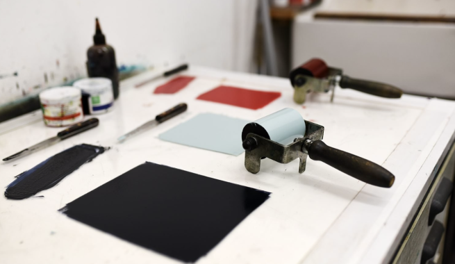 Ink rollers and black, blue and red inks being rolled out ready to be applied to lino