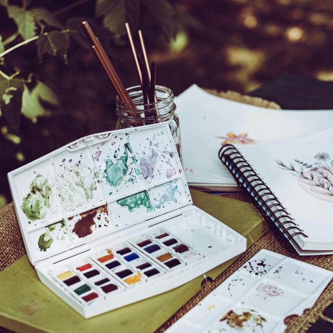 A watercolour palette next to an open sketchbook
