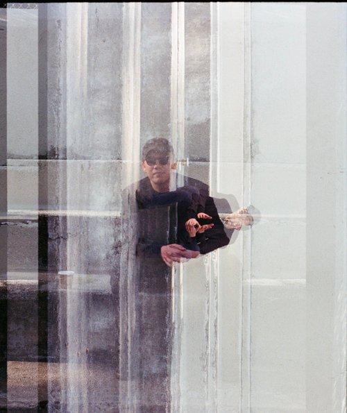 A triple exposure photograph of artist Sam Weinberg wearing sunglasses and a dark shirt sat on some stone stairs, the first is portrait and the other two are landscape.