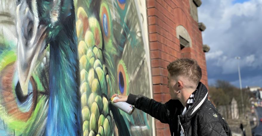 Artist CBLOXX painting a mural on a red brick wall