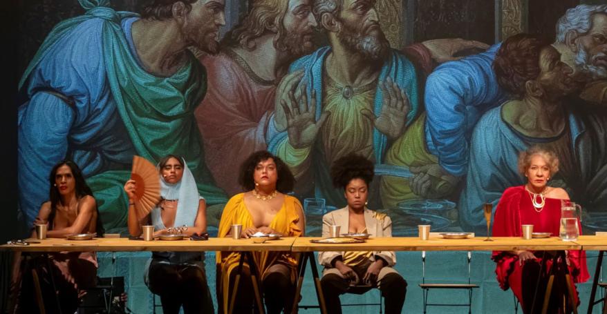 A reinterpretation of ‘The Last Supper’ painting with people gathered around a table. In the background, the original artwork. 