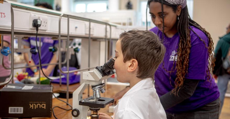 A volunteer helps a child look through a microscope