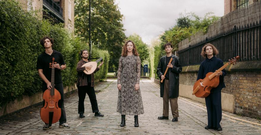Five musicians stood in a street hold their instruments. 