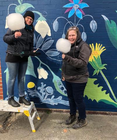 two women holding candy floss in front of the mural they are painting