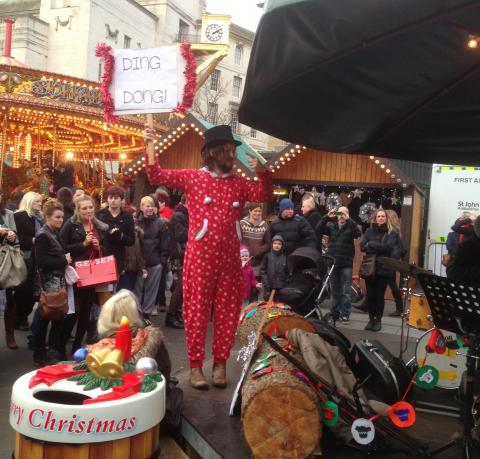 man on stage at a christmas market in a red christmas onesie