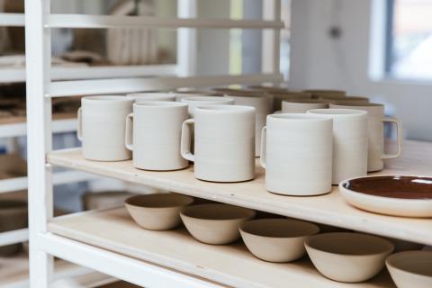 Unfired cylindrical mugs, and small dipping bowls on a pottery ware truck.