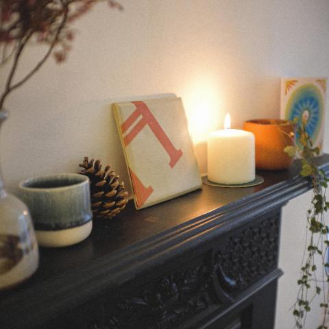 Decorative tile propped on a mantelpiece next to a candle and fir cone