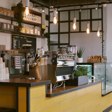 Image shows a coffee shop bar, with hanging lights and a coffee machine in the foreground.