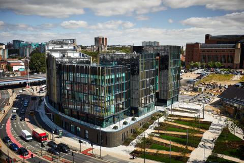 A big glass building next to a busy road with green gardens in front