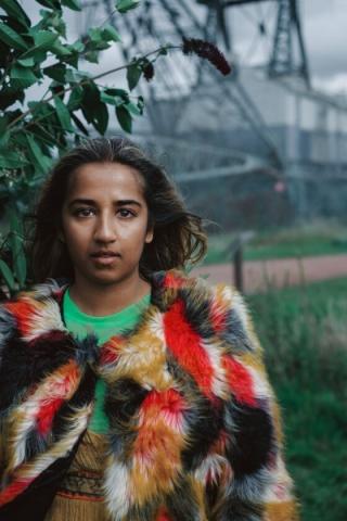 a young woman looks straight at the camera wearing a multi coloured coat