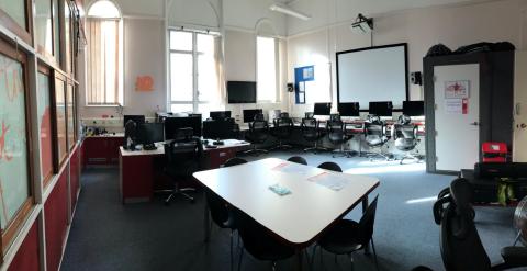 Studio 12, several Mac computers lined up against the wall, recording booth in the corner, a table in the foreground.