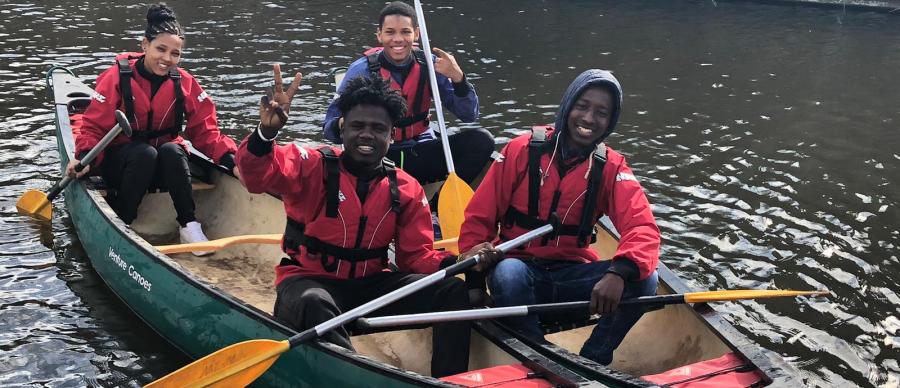 Four young people in life jackets, smiling on canoes