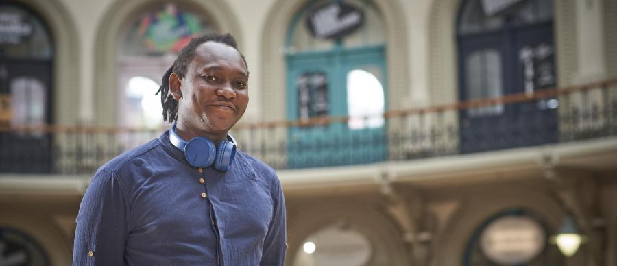 Musician Abel Selaocoe with headphones around his neck, standing in Leeds Corn Exchange