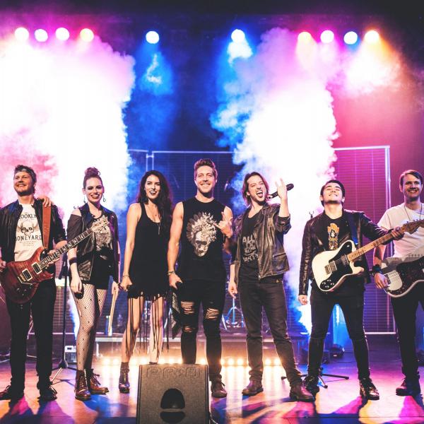 A group of rock musicians on a stage, some with guitars, others with microphones