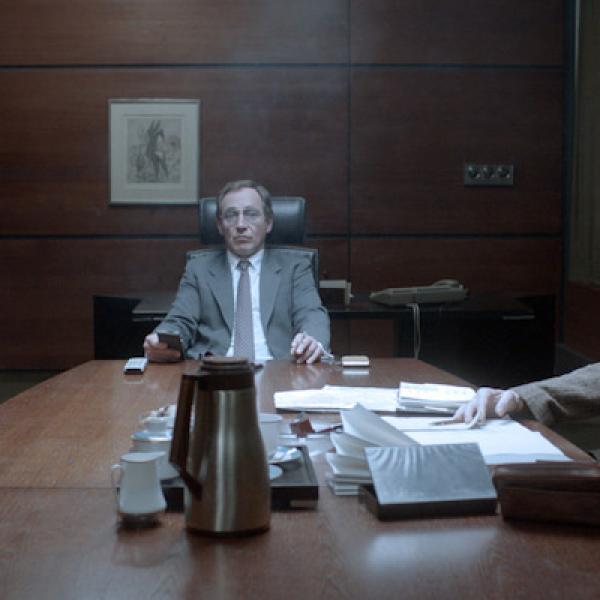 Picture shows 3 official looking men sat around a big table in a meeting