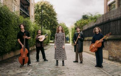Five musicians stood in a street hold their instruments. 