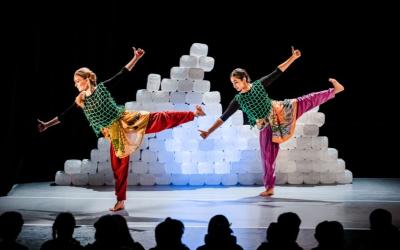 Two figures dancing on stage with a mountain of clear plastic tubs behind them. 