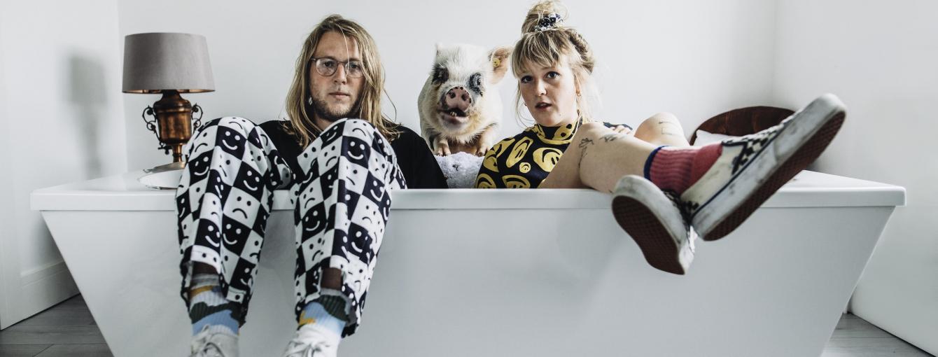 two members of the band in a bath fully dressed with a pig