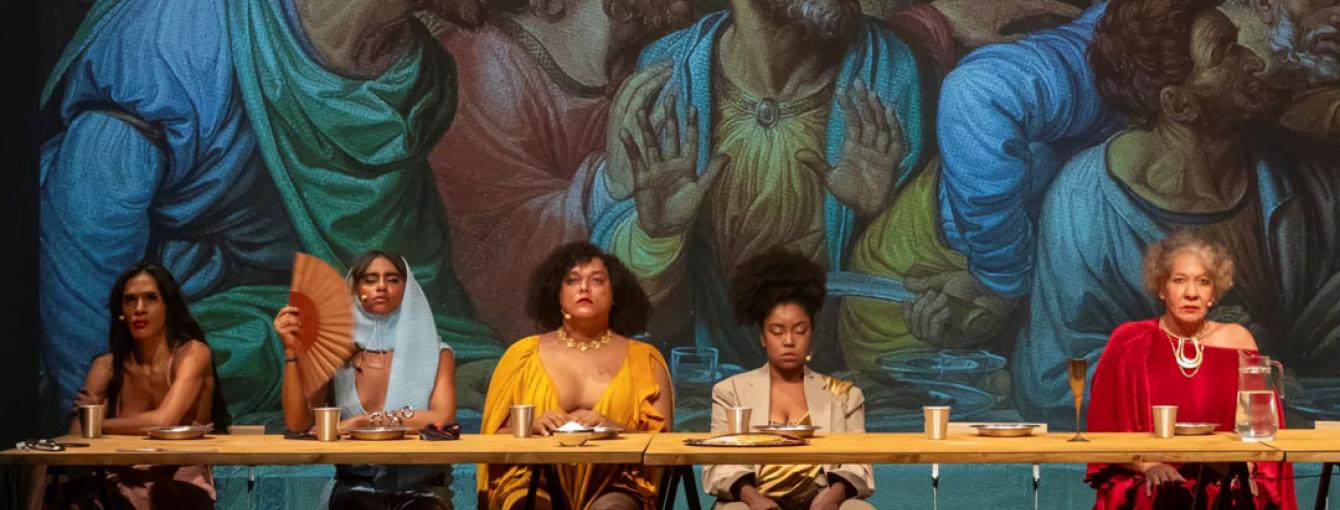 A reinterpretation of ‘The Last Supper’ painting with people gathered around a table. In the background, the original artwork. 