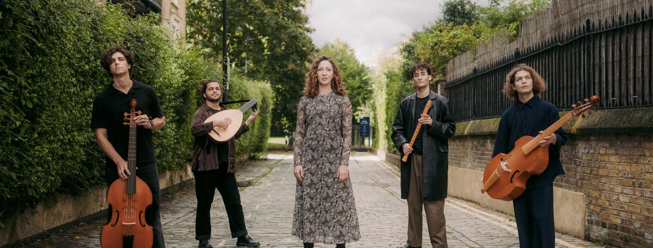 Five musicians standing in a street hold their instruments. 
