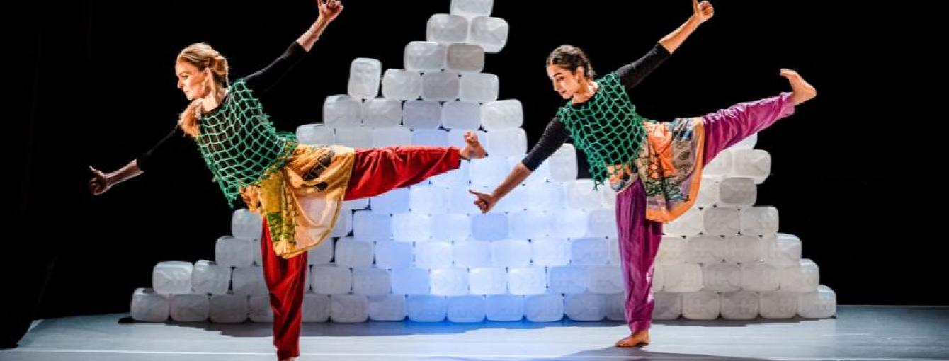 Two figures dancing on stage with a mountain of clear plastic tubs behind them. 